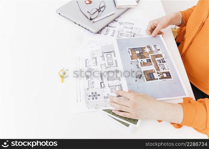 elevated view of female hand holding blueprint on white desk