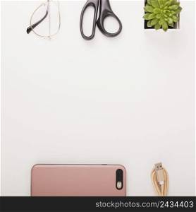 elevated view smartphone usb cable potted plant scissors spectacles white background