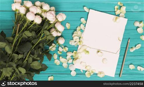 elevated view white roses pencil blank paper petals against green wooden table