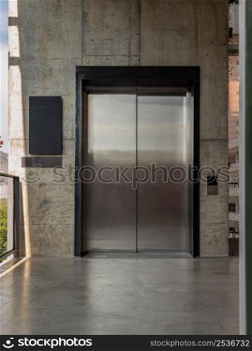 Elevator chrome metal with closed door on Bare cement wall for lifting people to the upper floors with push switch for up and down at modern building design. Selective focus.