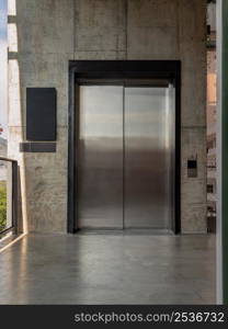 Elevator chrome metal with closed door on Bare cement wall for lifting people to the upper floors with push switch for up and down at modern building design. Selective focus.