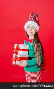 Elf girl with gifts, Santa Claus helper on a bright red bright colored background. Portrait of a beautiful elven baby. Copy space.. Elf girl with gifts, Santa Claus helper on a bright red bright colored background. Portrait of a beautiful elven baby.