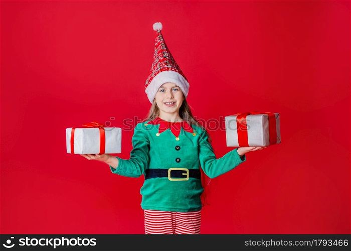 Elf girl with gifts, Santa Claus helper on a bright red bright colored background. Portrait of a beautiful elven baby. Copy space.. Elf girl with gifts, Santa Claus helper on a bright red bright colored background. Portrait of a beautiful elven baby.
