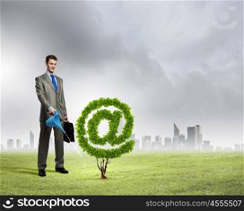 Email concept. Image of businessman watering plant shaped like at symbol