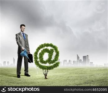 Email concept. Image of businessman watering plant shaped like at symbol