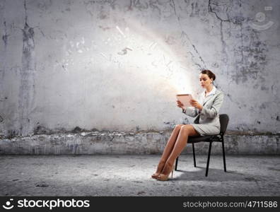 Email concept. Image of businesswoman sitting on chair with tablet pc in hands