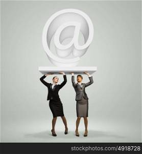 Email concept. Image of two businesswomen holding at symbol. Partner and cohesion