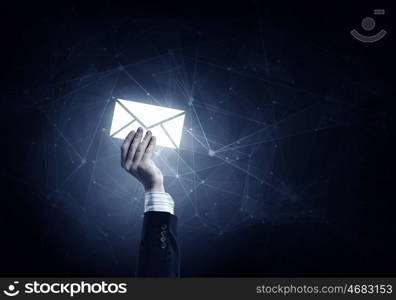 Email concept in hand. Businessman hand on dark background holding email glowing symbols