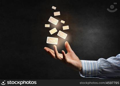 Email concept in hand. Businessman hand on dark background holding email symbols in palm