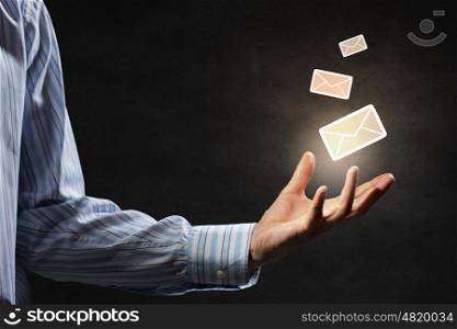 Email concept in hand. Businessman hand on dark background holding email symbols in palm