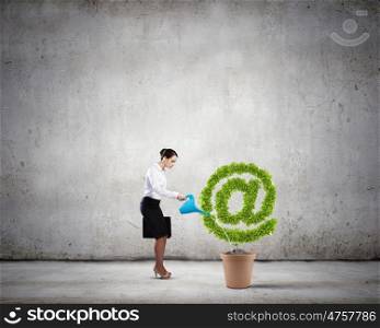 Email concept. Young attractive businesswoman watering plant in pot with can
