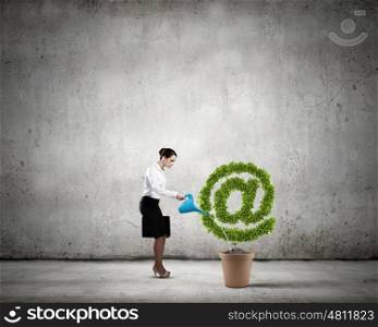 Email concept. Young attractive businesswoman watering plant in pot with can