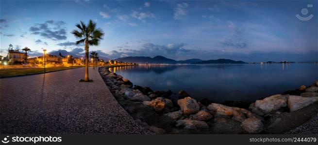 Embankment with a path and palm trees lit by lanterns in the early morning. Panorama. Fethiye, Turkey. Embankment lit by lanterns in early morning