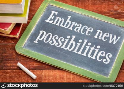 Embrace new possibilities - white chalk text on a slate blackboard with a stack of books against rustic wooden table