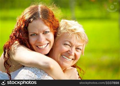 Embraces happy mothers with the adult daughter against a lawn
