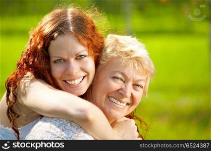 Embraces happy mothers with the adult daughter against a lawn. Family