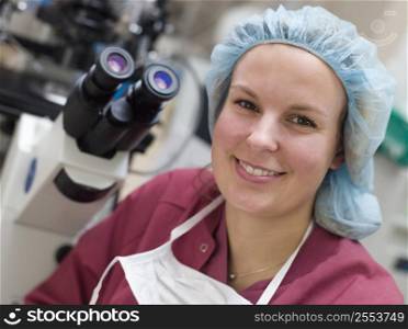 Embryologist sitting by microscope smiling (selective focus)