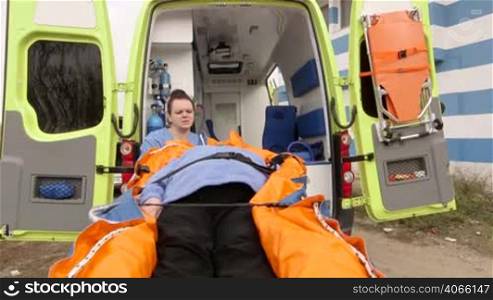 Emergency medical ambulance service paramedics crew fixing senior patient on stretcher collapsible vacuum mattress with safety belts