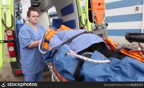Emergency medical ambulance service paramedics crew fixing senior patient on stretcher collapsible vacuum mattress with safety belts