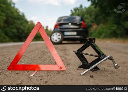 Emergency stop sign and lift jack, car breakdown. Broken automobile or repairing of flat tyre on vehicle, trouble with punctured auto tire on highway