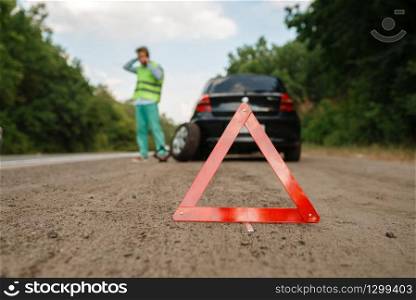 Emergency stop sign, car breakdown, man calling for tow truck on background. Broken automobile or repairing of flat tyre on vehicle, trouble with punctured auto tire on highway