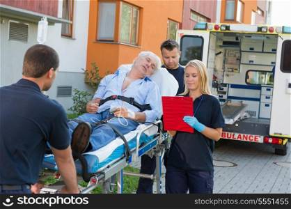 Emergency team assisting injured elderly man lying on stretcher outdoors