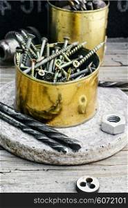 Emery wheel and a set of drill bits and screws on wooden background. Iron the jar of screws