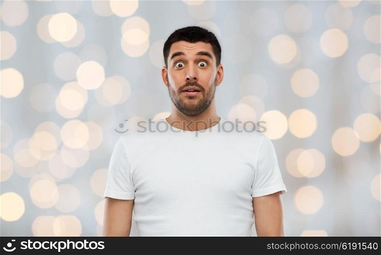 emotion, advertisement and people concept - scared man in white t-shirt over holidays lights background