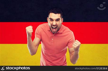emotion, aggression, gesture and people concept - angry young man or immigrant showing fists over german flag background. angry man showing fists over german flag