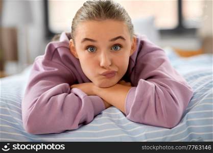 emotion, expression and people concept - girl lying on bed at home and making face. girl lying on bed at home and making face