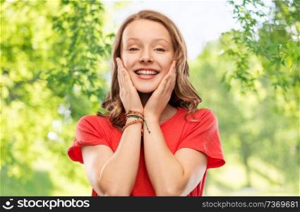 emotion, expression and people concept - happy smiling teenage girl with long hair in red t-shirt over green natural background. smiling teenage girl over natural background