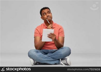 emotion, expression and people concept - pensive indian man in polo shirt with notebook and pen over gray background. indian man in polo shirt with notebook and pen