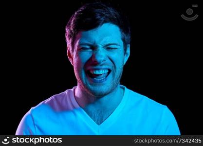 emotion, expression and people concept - portrait of laughing young man in t-shirt over ultra violet neon lights in dark room. man laughing over neon lights in dark room