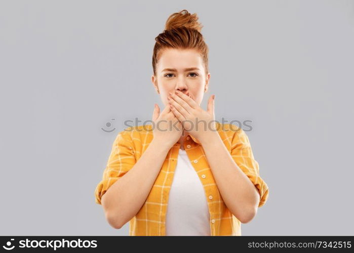 emotion, expression and people concept - red haired teenage girl in checkered shirt covering mouth by hands over grey background. red haired teenage girl covering mouth by hands