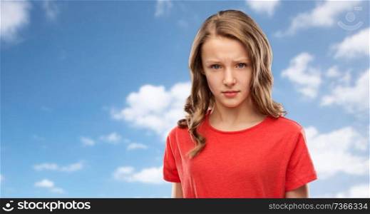 emotion, expression and people concept - sad or angry teenage girl in red t-shirt over blue sky and clouds background. sad or angry teenage girl in red t-shirt over sky