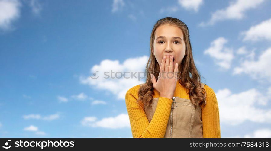 emotion, expression and people concept - scared or yawning teenage girl closing her mouth by hand over blue sky and clouds background. teenage girl closing her mouth by hand or yawning