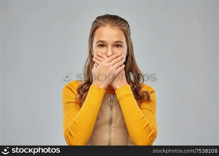 emotion, expression and people concept - scared teenage girl closing her mouth by hands over grey background. scared teenage girl closing her mouth by hands