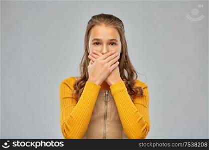 emotion, expression and people concept - scared teenage girl closing her mouth by hands over grey background. scared teenage girl closing her mouth by hands
