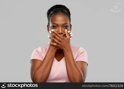 emotion, expression and people concept - shocked african american woman closing her mouth with hands over grey background. shocked african american woman covering her mouth