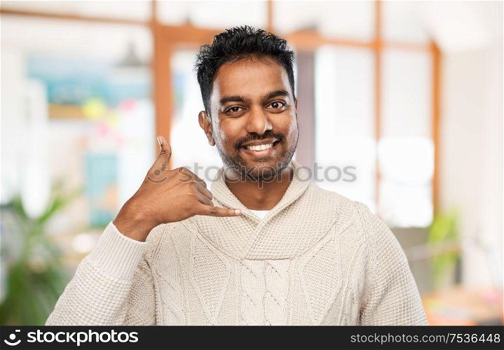emotion, expression and people concept - smiling indian man in knitted woolen sweater making phone call gesture over office background. indian man in sweater making phone call gesture