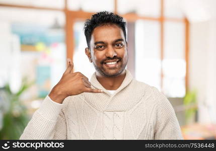 emotion, expression and people concept - smiling indian man in knitted woolen sweater making phone call gesture over office background. indian man in sweater making phone call gesture