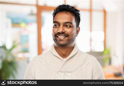 emotion, expression and people concept - smiling indian man in knitted woolen sweater over office background. indian man in sweater over office background