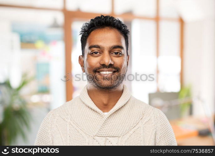 emotion, expression and people concept - smiling indian man in knitted woolen sweater over office background. indian man in sweater over office background