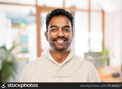 emotion, expression and people concept - smiling indian man in knitted woolen sweater over office background. indian man in sweater over office background