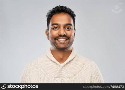emotion, expression and people concept - smiling indian man in knitted woollen sweater over gray background. indian man in knitted sweater over gray background