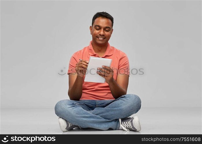 emotion, expression and people concept - smiling indian man in polo shirt writing to notebook over gray background. indian man in polo shirt writing to notebook