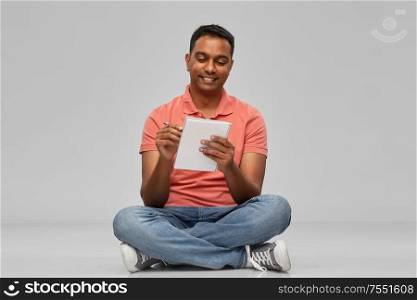 emotion, expression and people concept - smiling indian man in polo shirt writing to notebook over gray background. indian man in polo shirt writing to notebook