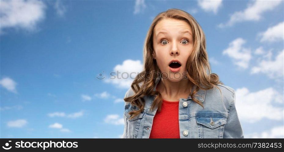 emotion, expression and people concept - surprised or shocked teenage girl with open mouth over blue sky and clouds background. surprised or shocked teenage girl over sky