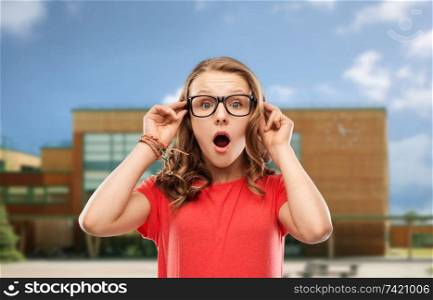 emotion, expression and people concept - surprised or shocked teenage girl with open mouth in glasses over school background. surprised teenage girl in glasses over school