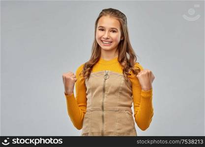 emotion, expression and success concept - happy smiling young teenage girl celebrating triumph over grey background. happy young teenage girl celebrating success